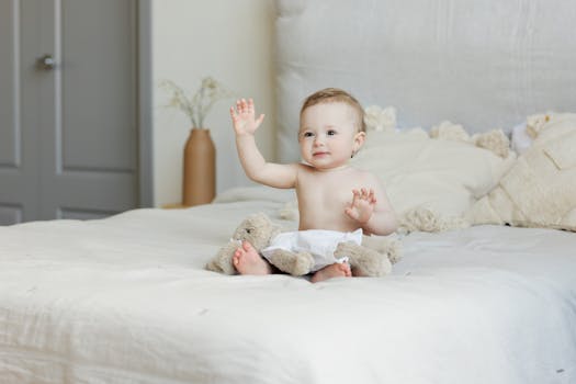 A cute baby happily sitting on a bed with plush toys, radiating a joyful expression.
