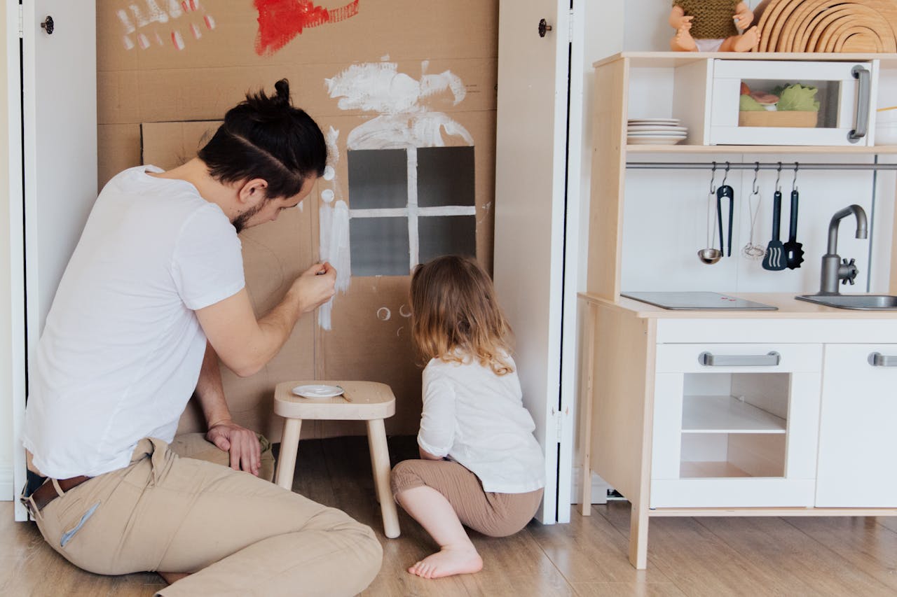 Tracking Tiny Talkers: Communication A father and child enjoying creative painting time indoors with a cardboard house.