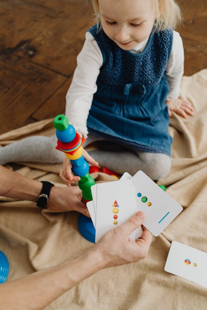 pexels photo 7296431 A young girl enjoying a colorful educational stacking toy game with a parent's help indoors.