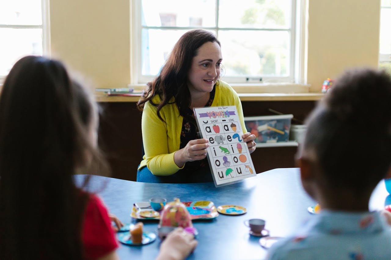 November 2025 Teacher engaging young children in a fun learning activity with phonics chart in a classroom setting.