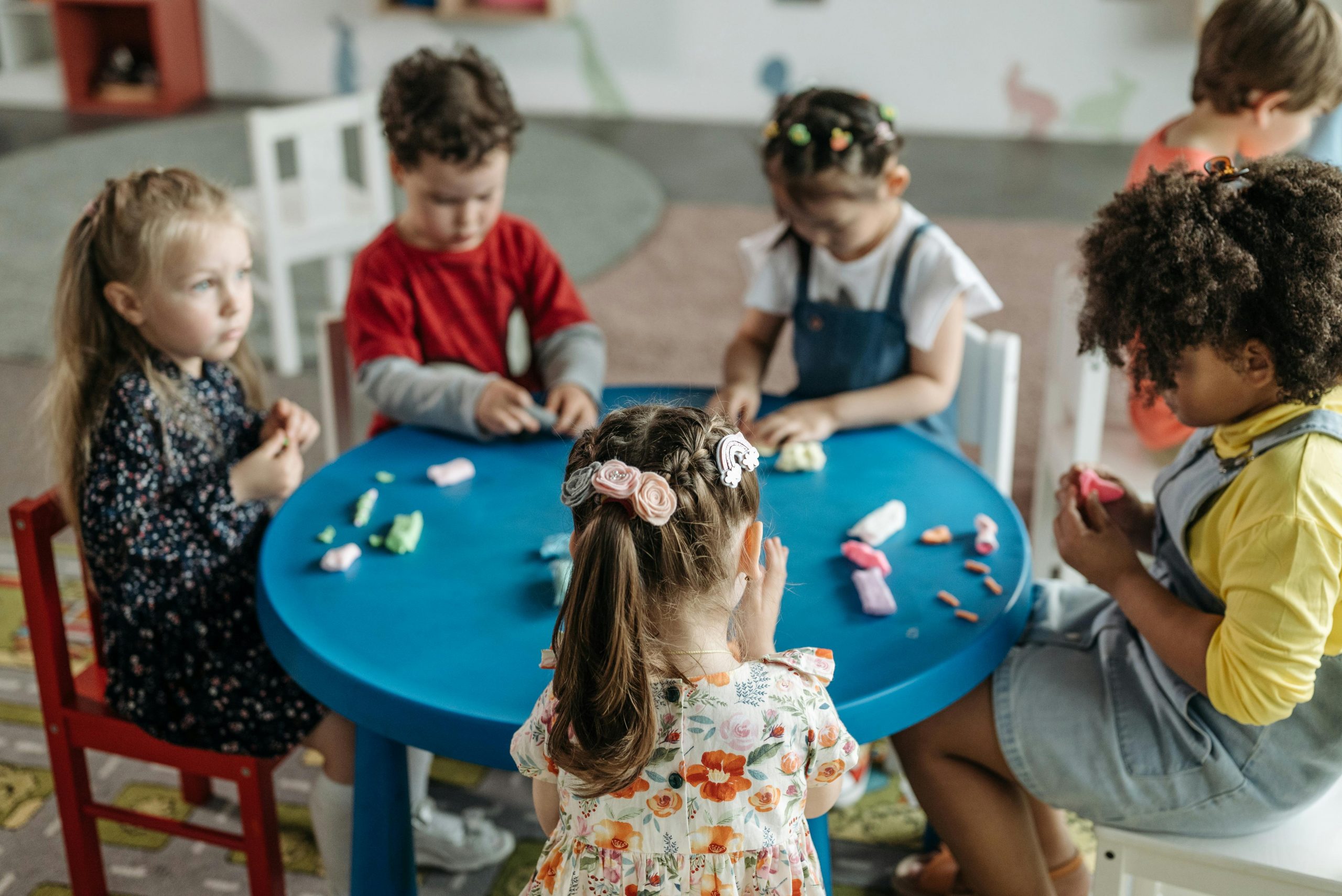 Raising Bilingual Communicators Group of preschool children playing with clay at a colorful table in a classroom.