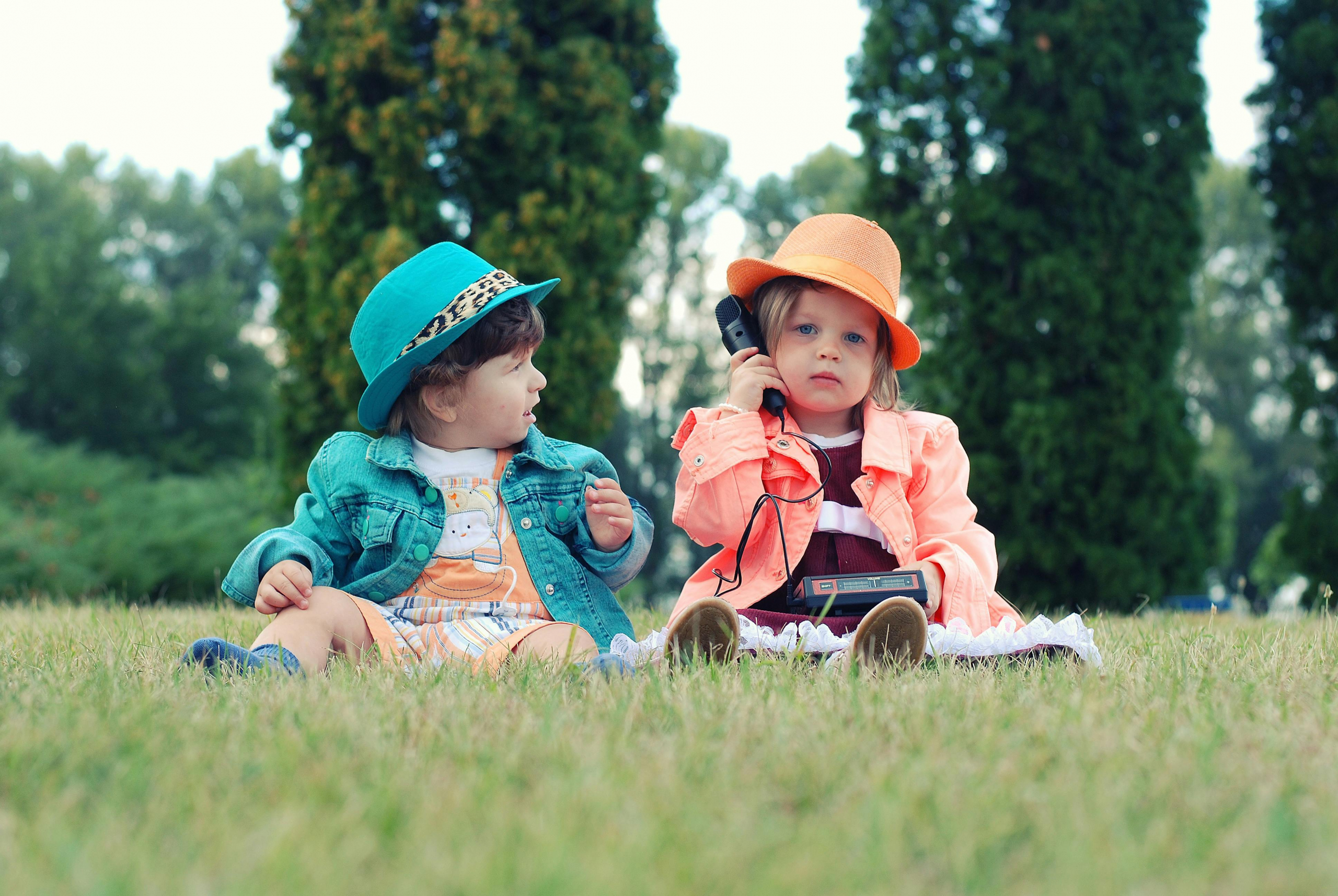 Speech Sound Acquisition: What Research Tells Us Two toddlers in colorful outfits enjoying playtime with walkie talkies in a sunny park setting.
