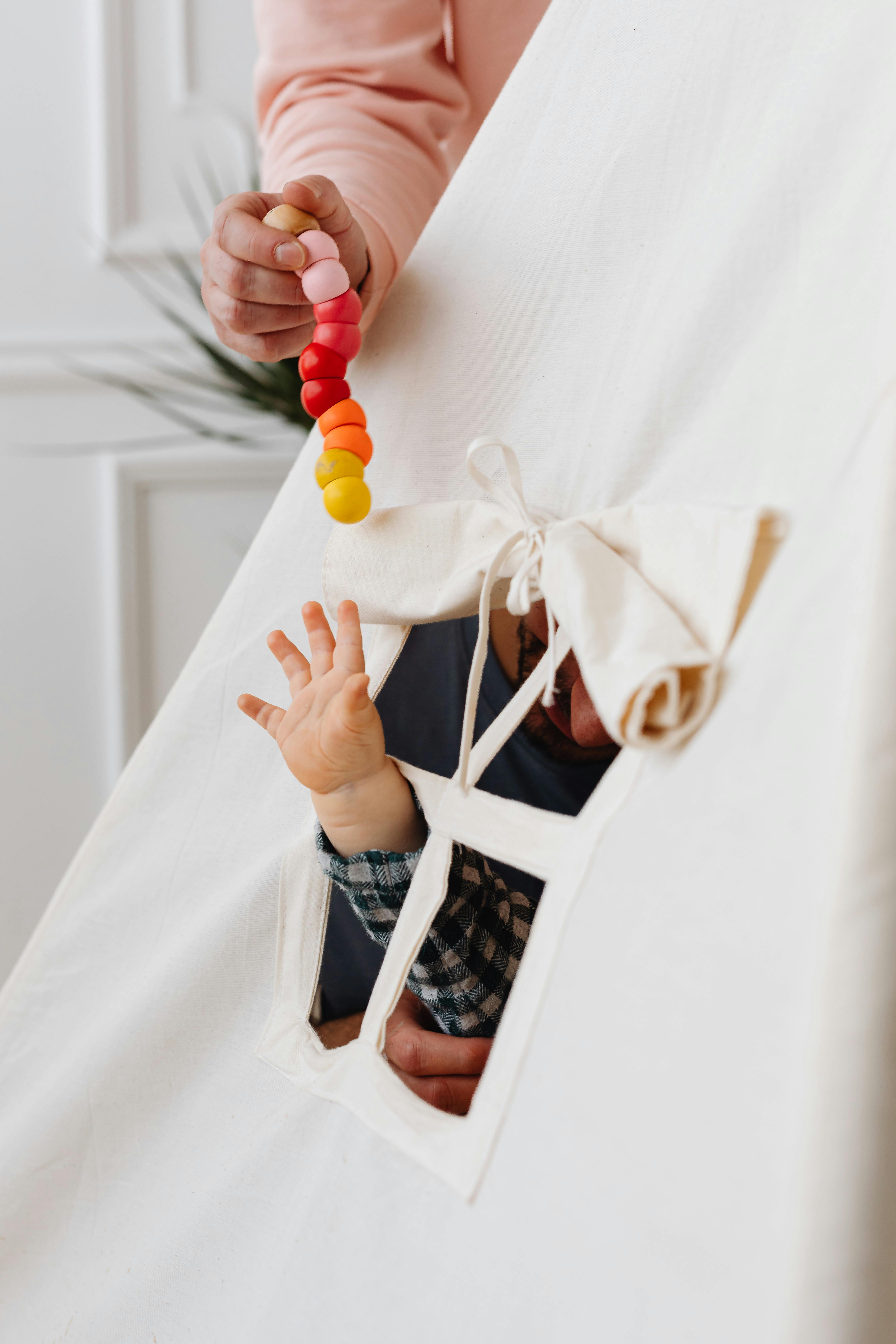 Why Gestures Matter: Supporting Your Toddler’s Communication A baby's hand reaching out from a teepee tent window to grab a colorful toy.