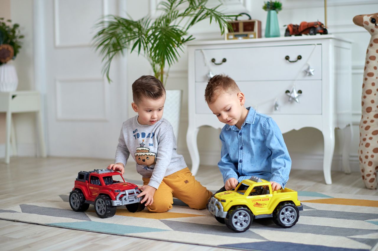 Two young boys enjoying indoor play with toy trucks in a cozy room.