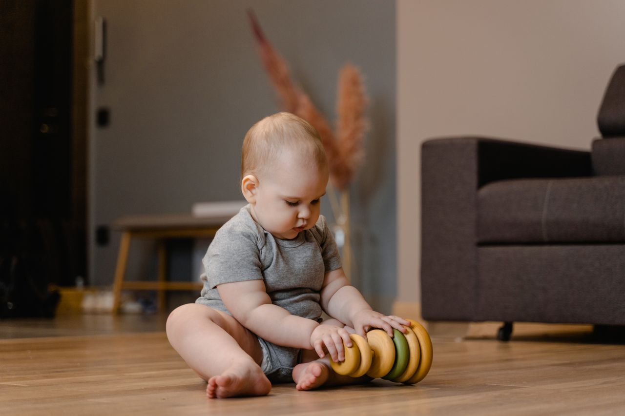 Cute baby playing with a wooden stacking toy indoors on a wooden floor.
