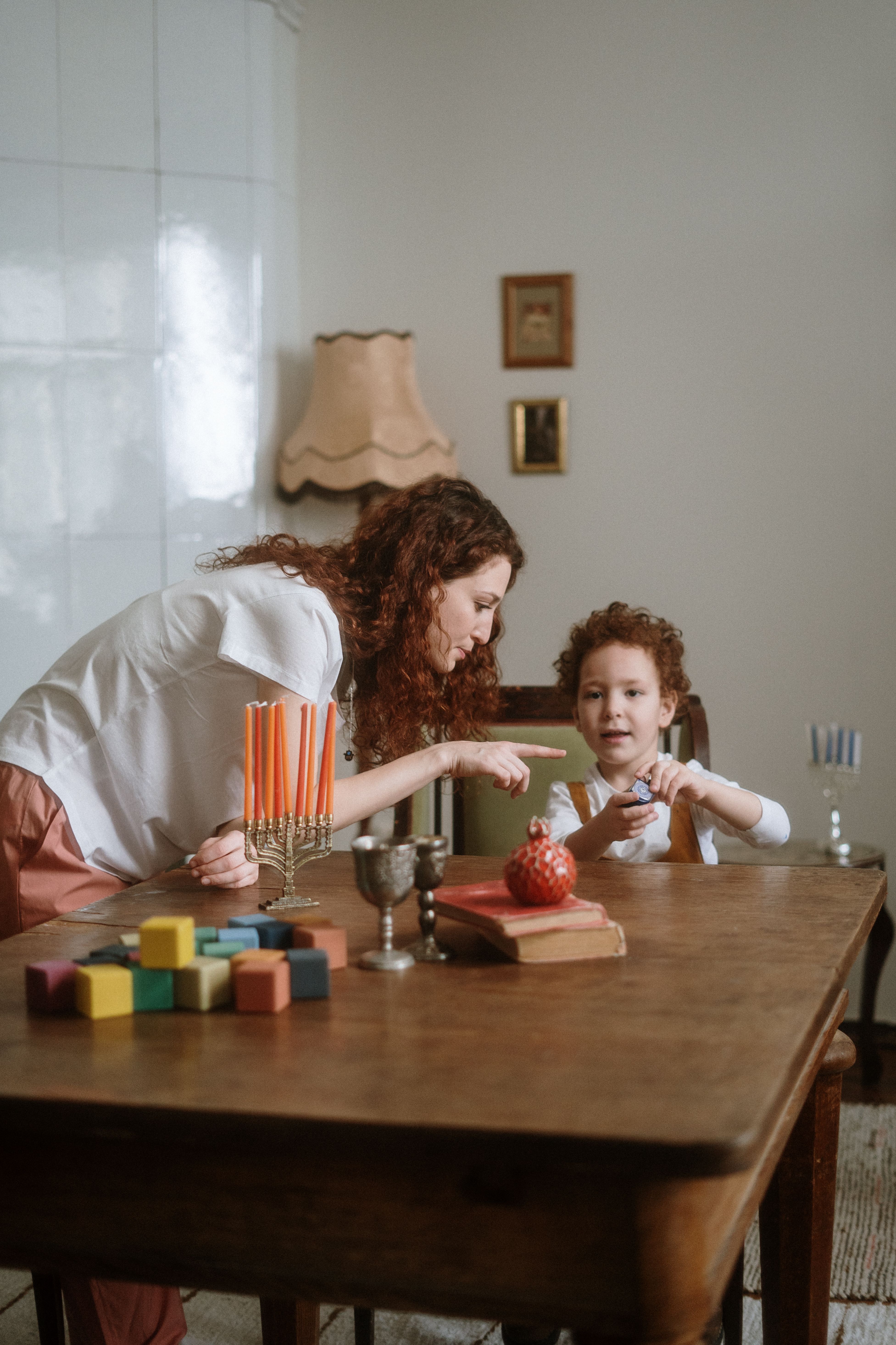 A mother and child engage in Hanukkah traditions with a menorah indoors.